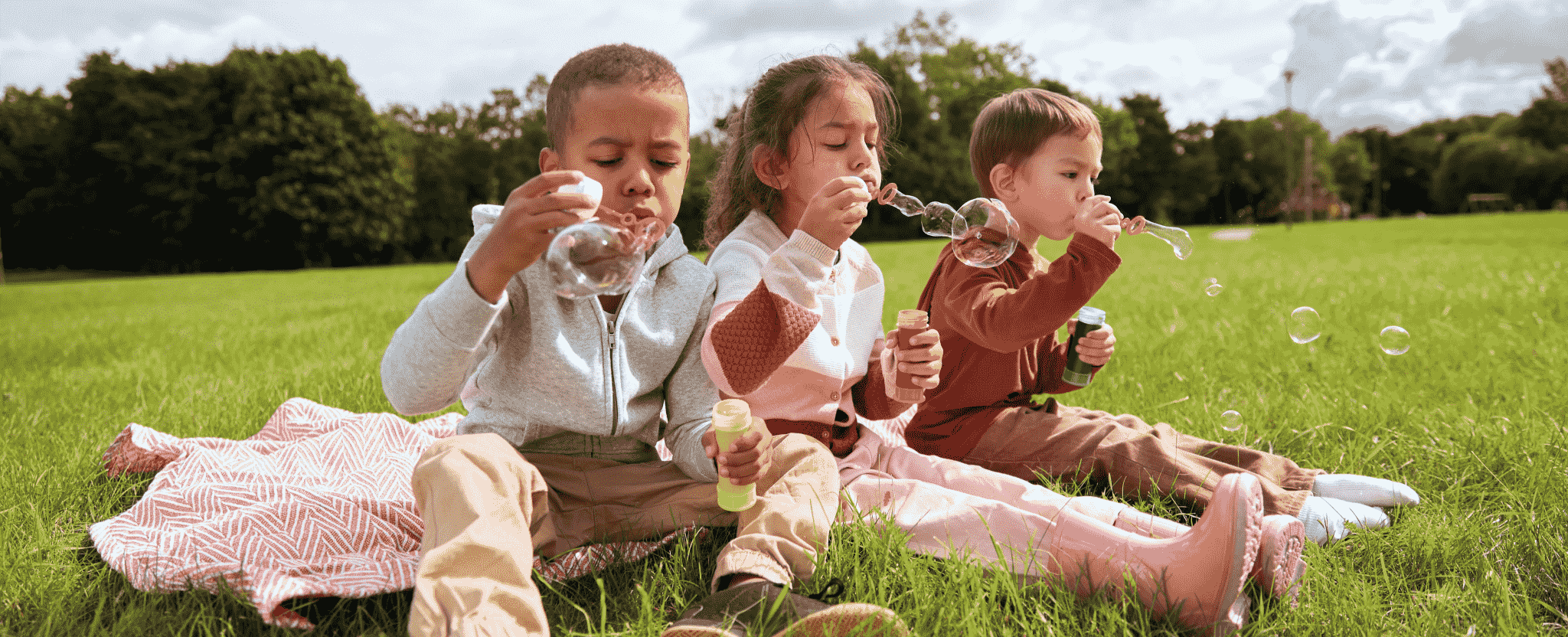 A group of happy children play outside, blowing bubbles.