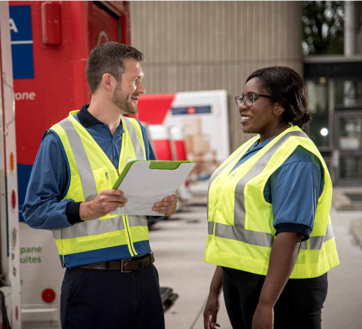 Un employé et une employée de Postes Canada vêtus d’un gilet de haute visibilité jaune discutent dans une installation de Postes Canada 