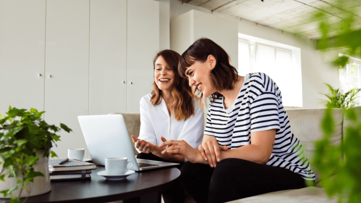 Two women smile as they look at a laptop together.