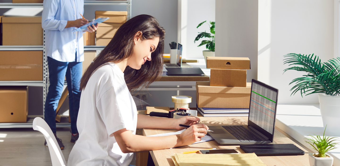 Une femme assise à un bureau écrit sur un bloc de papier devant un ordinateur portable.