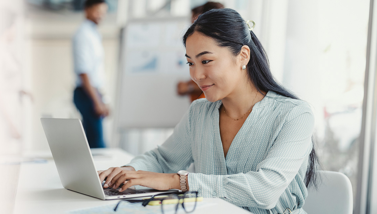 Une femme assise à une table de travail utilise un ordinateur portable