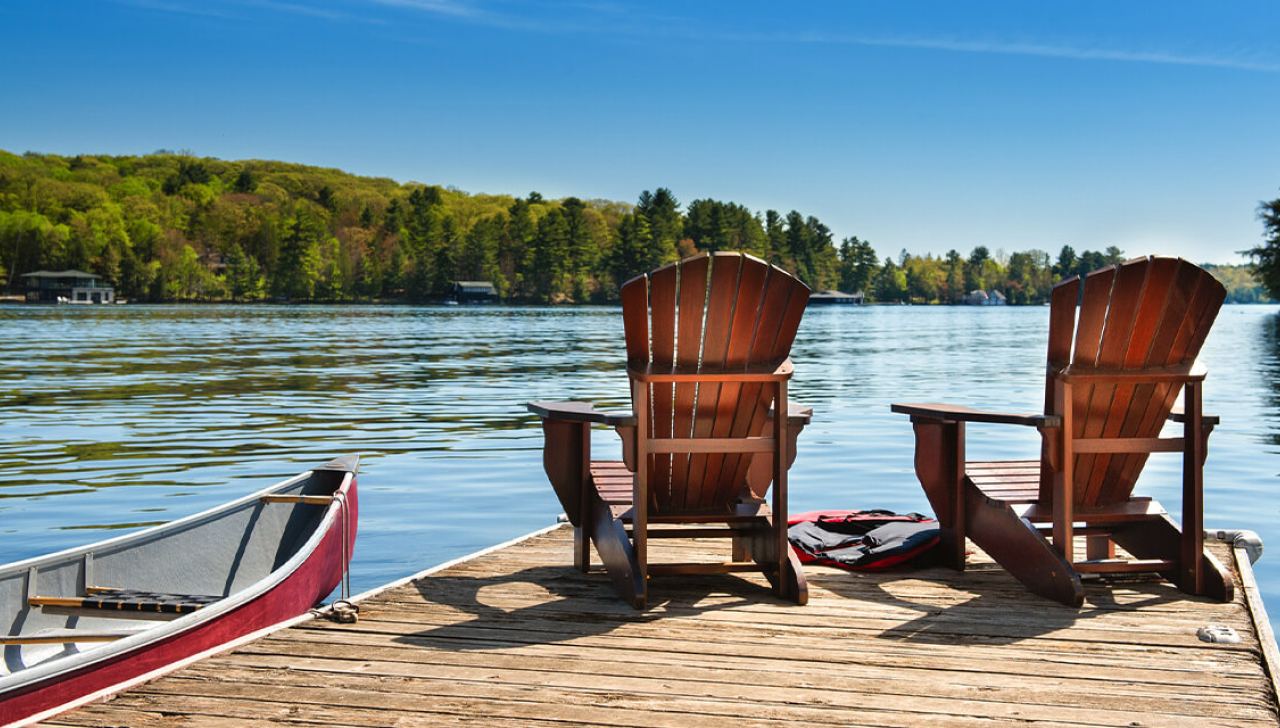 Deux chaises en bois reposent sur un quai au bord d’un lac, à côté d’un canot