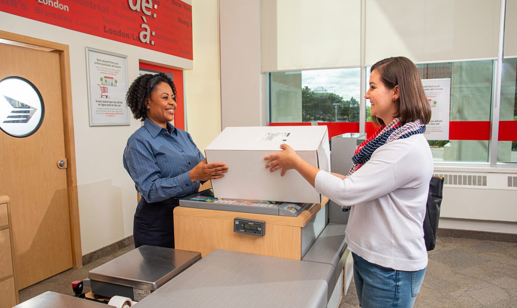 Une employée de Postes Canada sourit et remet un colis à une cliente souriante.