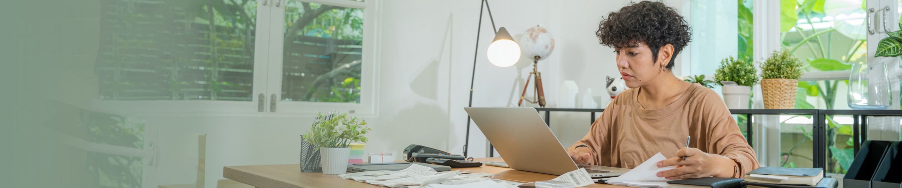 Une femme est assise à un bureau où elle travaille sur un ordinateur portable en feuilletant des documents.