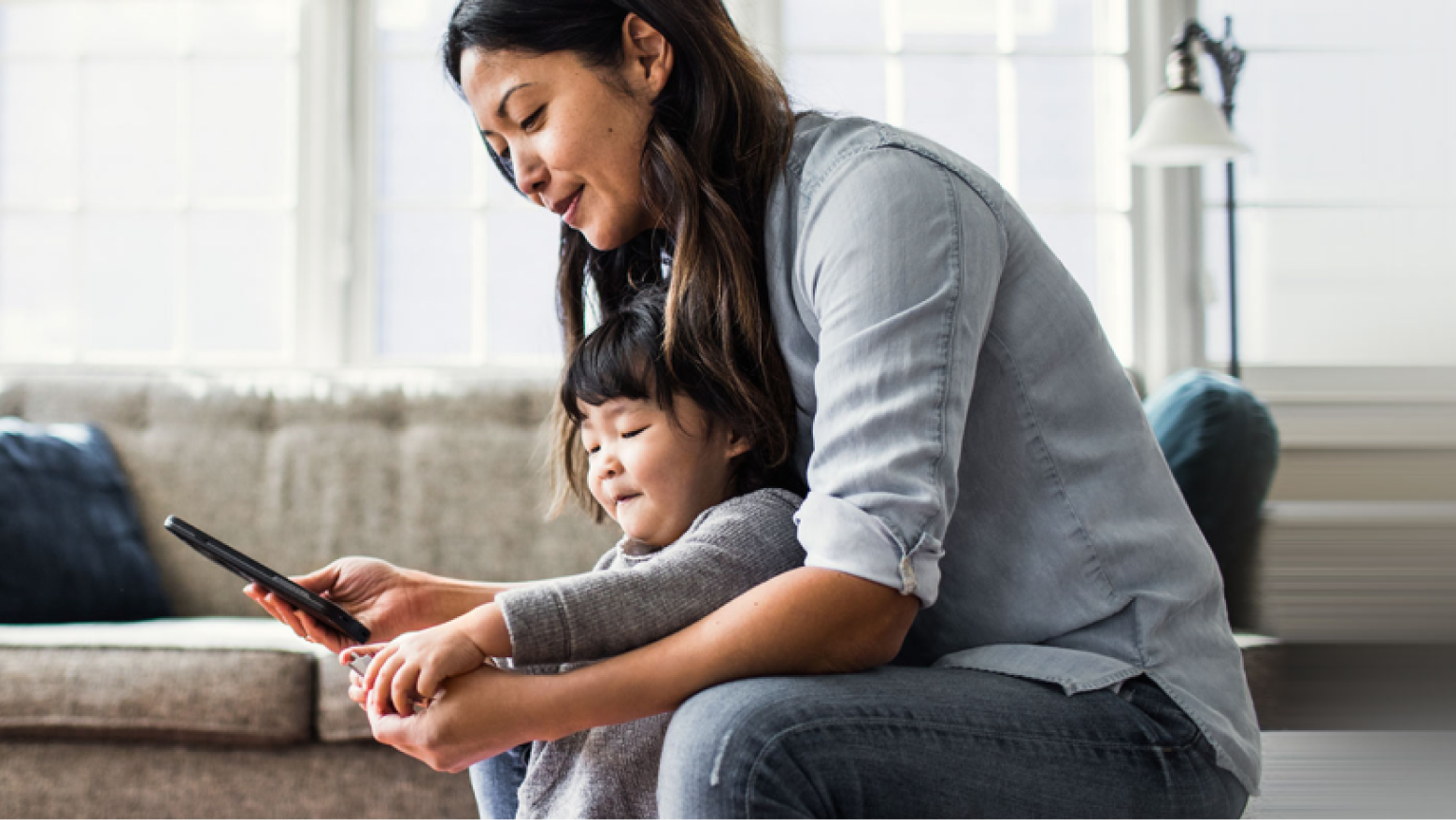 Femme qui consulte son téléphone cellulaire dans son salon en compagnie de son enfant.